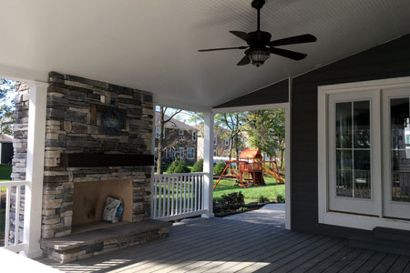 Covered porch with white columns, railings and a stone chimney